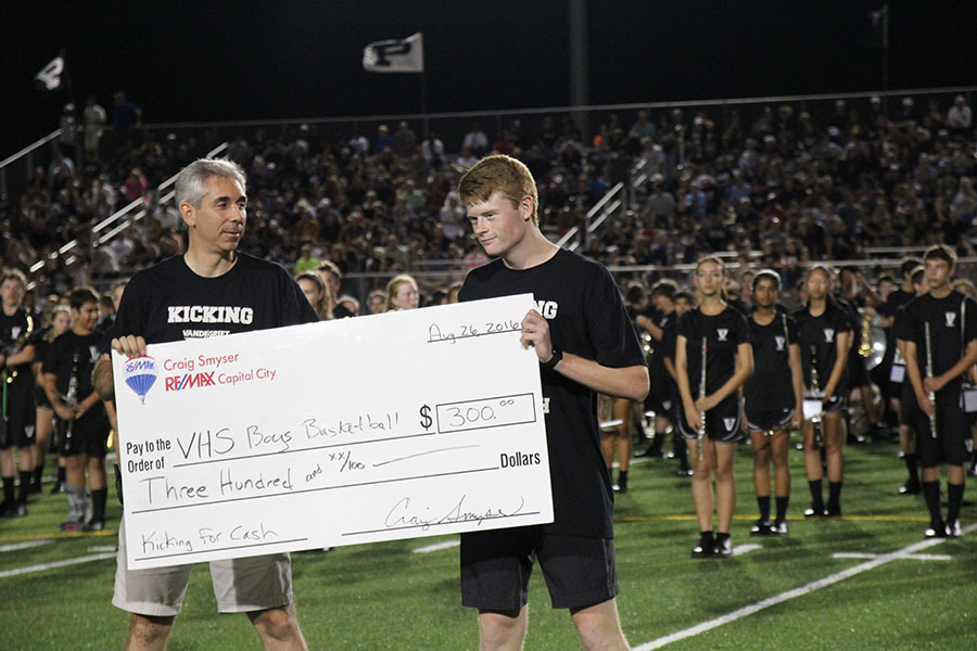 Alex Stadthaus accepts check for winning Kicking for Cash, representing the basketball team