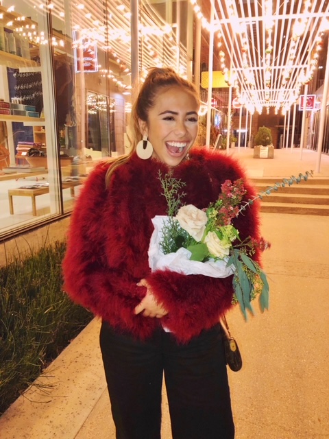 Alex at a Kendra Scott event, holding flowers and is modeling some Kendra Scott earrings, super proud of what she has done and accomplished