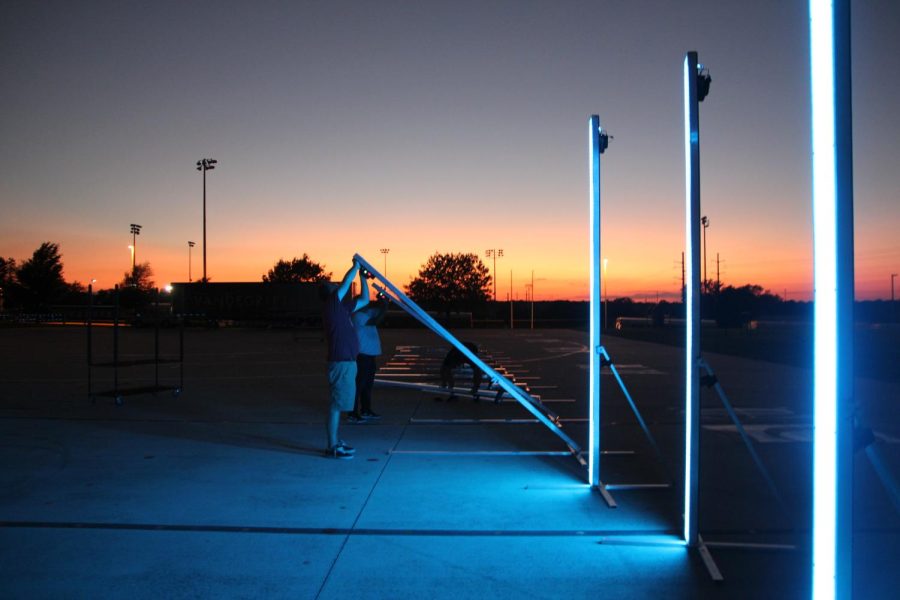 A team of prop parents work on various repairs past sunset. During the marching show these glowing poles light up and change color simultaneously.
