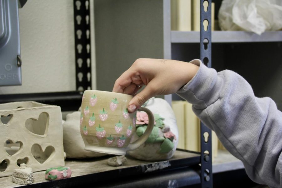 Barber shows off her older work, a strawberry mug. It sits towards the back of the shelf.
I keep them or give them away to people. Barber said. I go up to a lot of my family and am like here, take the pots.