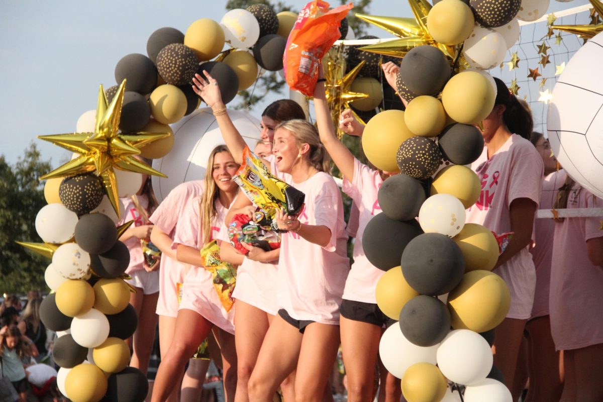 Beneath their net, varsity volleyball and senior Alexis Beauchamp throw candy during the Homecoming parade around the school.