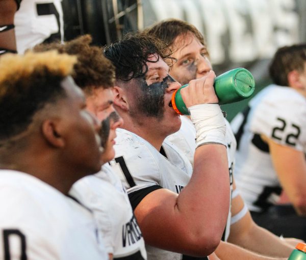 Junior defensive linemen Ian Witt squeezes water into his mouth while recovering on the bench during the varsity football game.