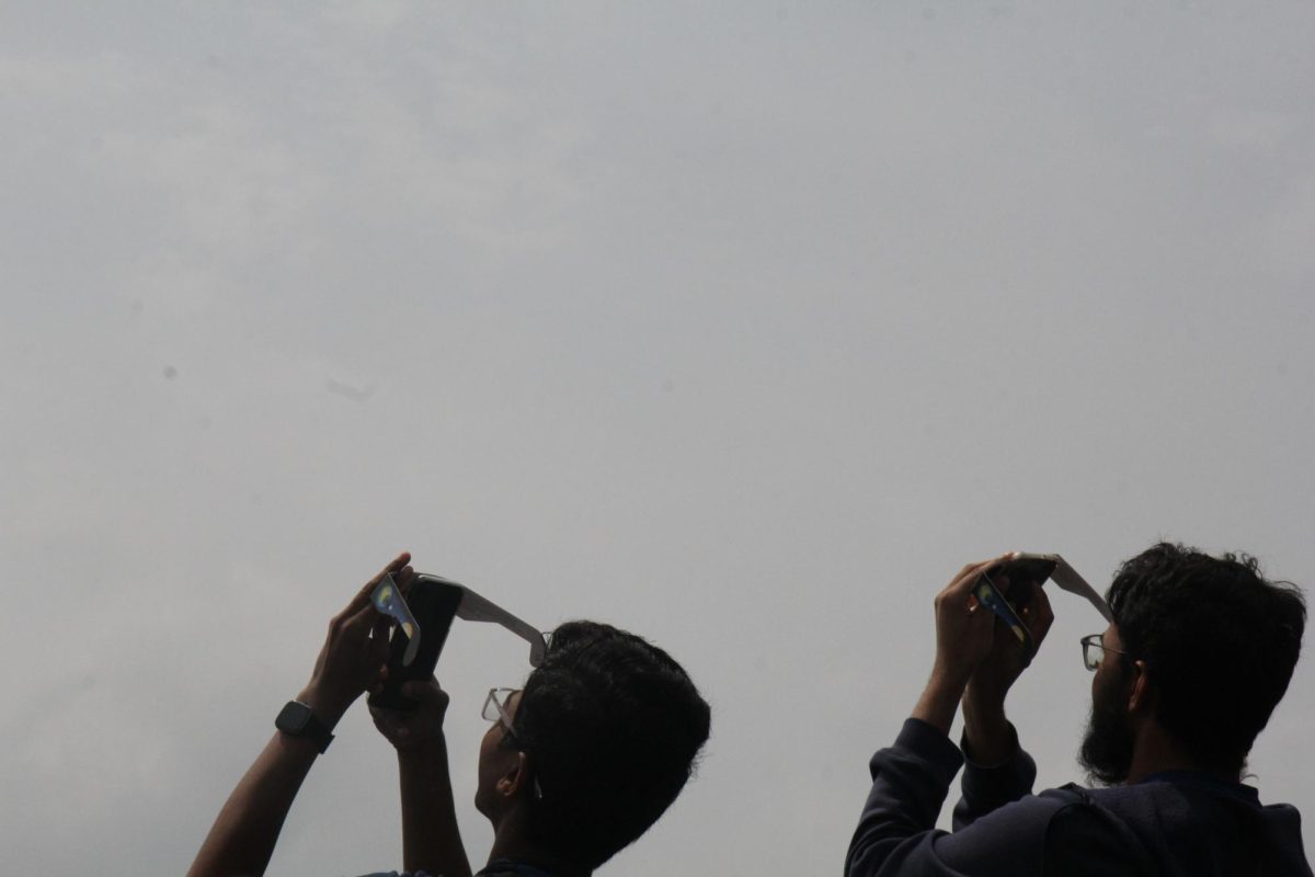 Two students take a picture of the solar eclipse using their eclipse glasses as solar filters. 