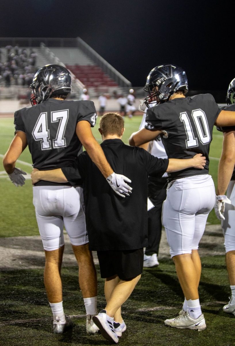  Mudlaff puts his arms around seniors Thomas Foote and Jack Clinkenbeard before a kickoff against Manor on Oct. 16 2025.